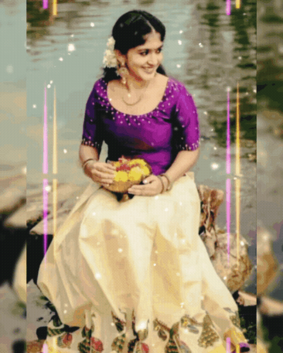 A Woman In A Purple Top And White Skirt Is Sitting On A Rock In The Water GIF