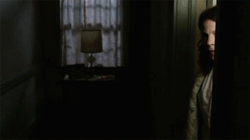 A Woman In A Quilted Robe Stands In A Dark Room GIF
