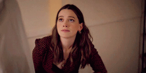 A Woman In A Red And Black Polka Dot Shirt Is Looking Up At The Sky . GIF