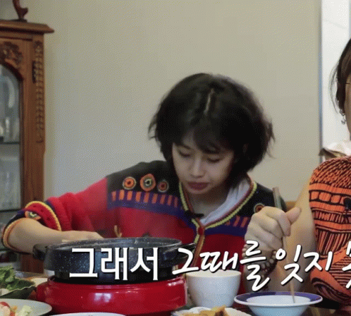 A Woman In A Red And Black Sweater Is Sitting At A Table With Plates Of Food And Chopsticks GIF