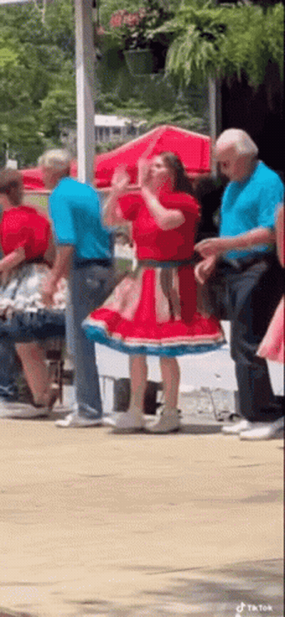 A Woman In A Red And Blue Dress Is Dancing With A Group Of People . GIF
