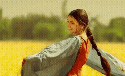 A Woman In A Red And Blue Dress Is Standing In A Field Of Yellow Flowers GIF