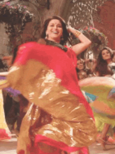 A Woman In A Red And Gold Dress Is Dancing In Front Of A Group Of People . GIF