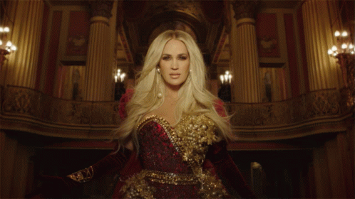 A Woman In A Red And Gold Dress Is Standing In A Room With Columns GIF
