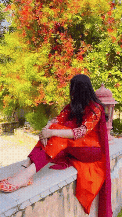 A Woman In A Red And Orange Dress Is Sitting On A Wall . GIF