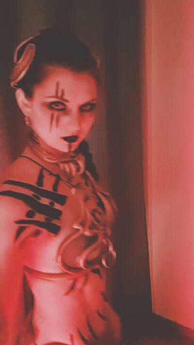 A Woman In A Red And White Costume With A Necklace Around Her Neck GIF