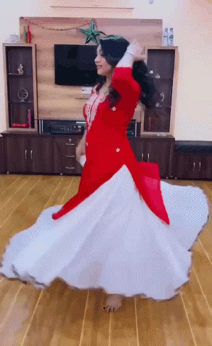 A Woman In A Red And White Dress Is Dancing In Front Of A Flat Screen Tv . GIF