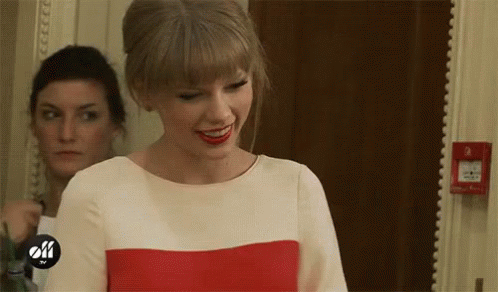 A Woman In A Red And White Dress Is Smiling In A Room . GIF