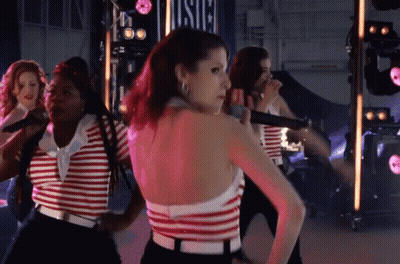 A Woman In A Red And White Striped Top Is Standing In Front Of A Sign That Says Usic GIF