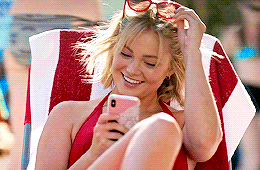 A Woman In A Red Bikini Is Sitting In A Chair Looking At Her Phone . GIF