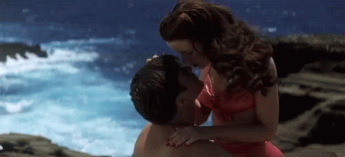 A Woman In A Red Bikini Kisses A Man On A Beach GIF