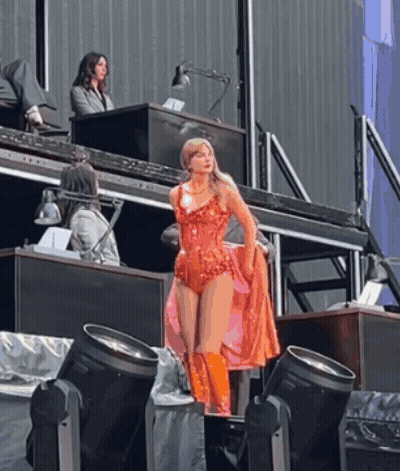 A Woman In A Red Bodysuit And Orange Boots Is Standing On A Stage GIF