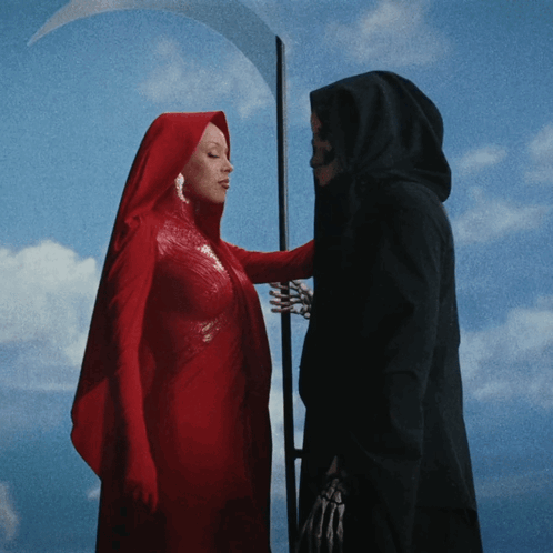 A Woman In A Red Cape Stands Next To A Grim Reaper With A Scythe GIF