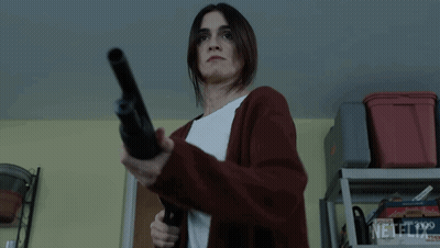 A Woman In A Red Cardigan Is Holding A Shotgun In A Garage . GIF
