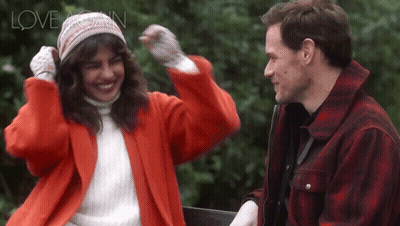 A Woman In A Red Coat And A Man In A Plaid Jacket Are Standing Next To Each Other And The Words Love Again Are Above The GIF
