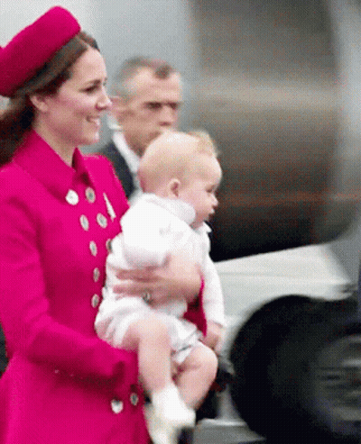 A Woman In A Red Coat Is Holding A Baby In Her Arms GIF