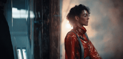 A Woman In A Red Coat Is Standing In Front Of A Window . GIF