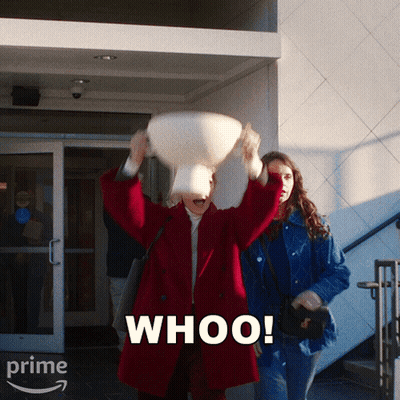 A Woman In A Red Coat Is Throwing A Pillow In The Air And The Word Whoo Is On The Bottom Right GIF