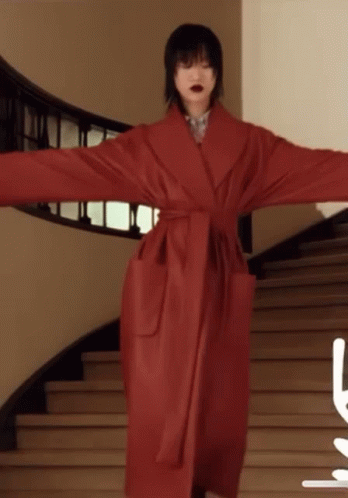 A Woman In A Red Coat Stands On A Set Of Stairs With Her Arms Outstretched GIF
