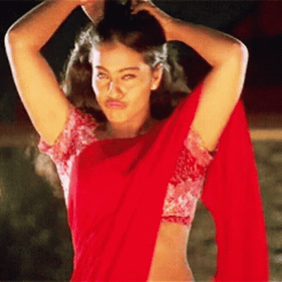 A Woman In A Red Crop Top And A Red Saree Is Standing With Her Arms In The Air . GIF