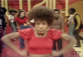 A Woman In A Red Crop Top Is Standing In Front Of A Crowd Of People Dancing . GIF
