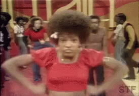 A Woman In A Red Crop Top Is Standing In Front Of A Crowd Of People Dancing . GIF