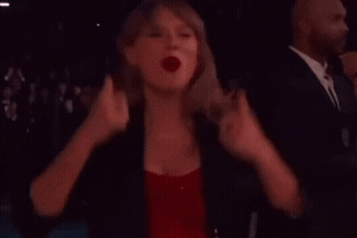 A Woman In A Red Dress And A Black Jacket Is Standing In A Dark Room . GIF