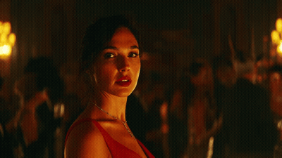 A Woman In A Red Dress And A Diamond Necklace Looks At The Camera GIF