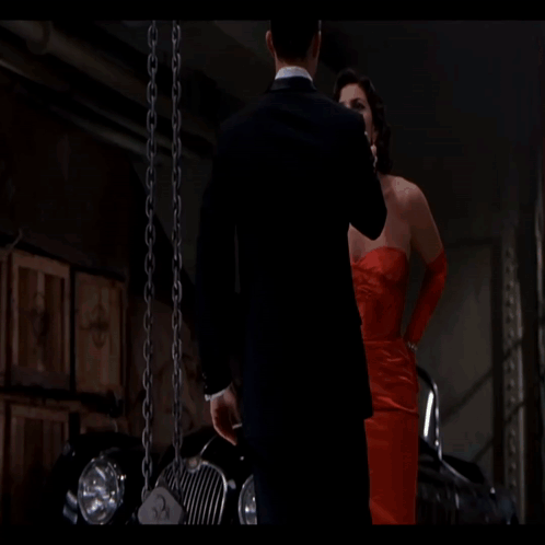 A Woman In A Red Dress And A Man In A Tuxedo Are Standing Next To Each Other GIF