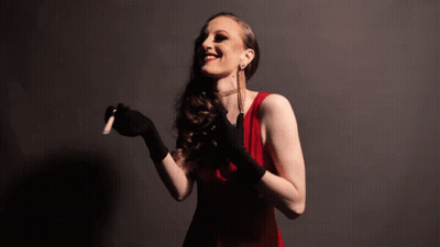 A Woman In A Red Dress And Black Gloves Is Holding A Cigarette GIF