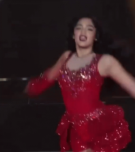 A Woman In A Red Dress And Boots Is Dancing On A Stage GIF