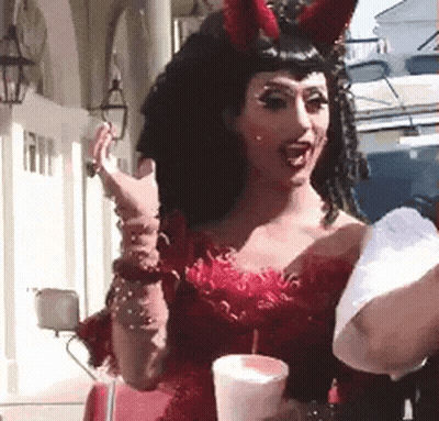 A Woman In A Red Dress And Devil Horns Is Holding A Cup . GIF