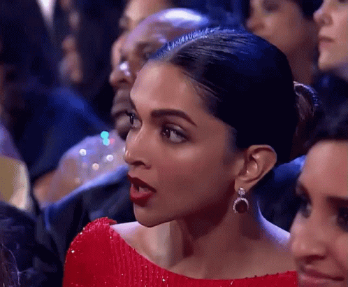 A Woman In A Red Dress And Earrings Is Sitting In A Crowd . GIF