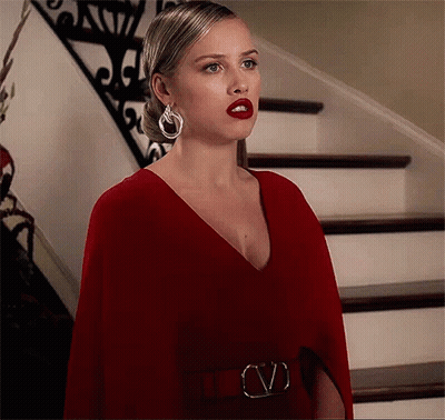 A Woman In A Red Dress And Earrings Is Standing In Front Of Stairs . GIF