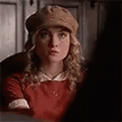 A Woman In A Red Dress And Hat Is Looking At The Camera . GIF