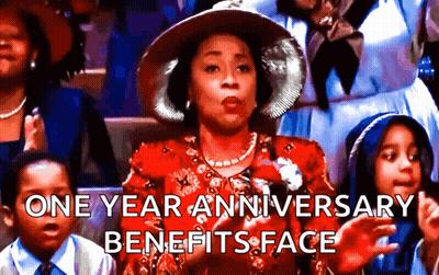 A Woman In A Red Dress And Hat Is Sitting In A Crowd And Says One Year Anniversary Benefits Face .. GIF