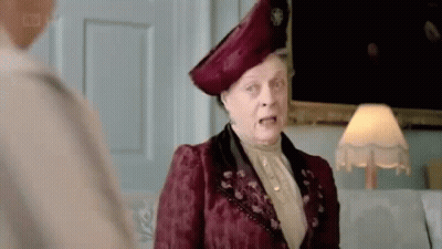 A Woman In A Red Dress And Hat Is Standing Next To A Lamp And Talking To Another Woman . GIF
