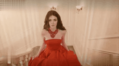 A Woman In A Red Dress And Necklace Is Sitting On A Set Of Stairs GIF