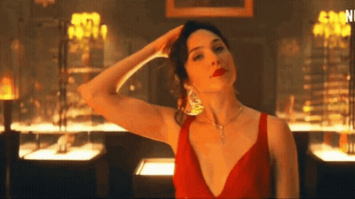A Woman In A Red Dress And Necklace Is Standing In A Room With Her Hand On Her Head . GIF