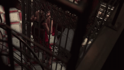 A Woman In A Red Dress Is Behind Bars In A Dark Room GIF