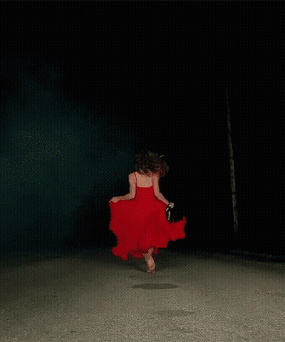 A Woman In A Red Dress Is Dancing Barefoot In The Dark GIF