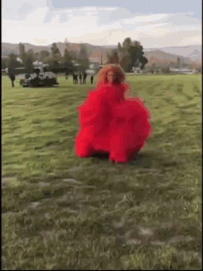 A Woman In A Red Dress Is Dancing In A Field . GIF