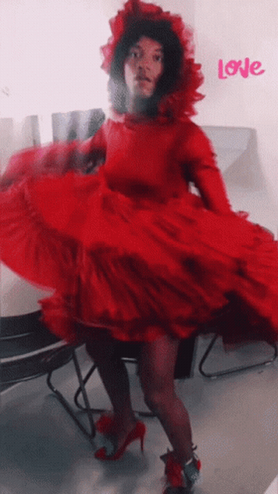 A Woman In A Red Dress Is Dancing In Front Of A Wall That Says Love GIF