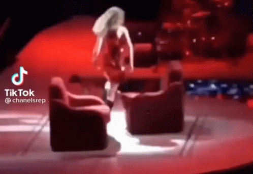 A Woman In A Red Dress Is Dancing On A Stage In Front Of Two Red Chairs . GIF