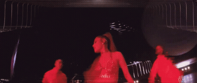 A Woman In A Red Dress Is Dancing On A Stage With A Man In A Red Shirt Behind Her GIF