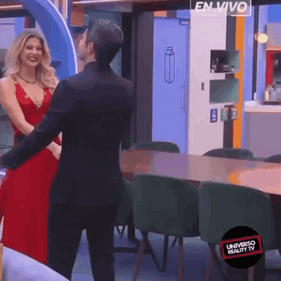 A Woman In A Red Dress Is Dancing With A Man In A Black Suit In A Room That Says Universo Reality Tv GIF