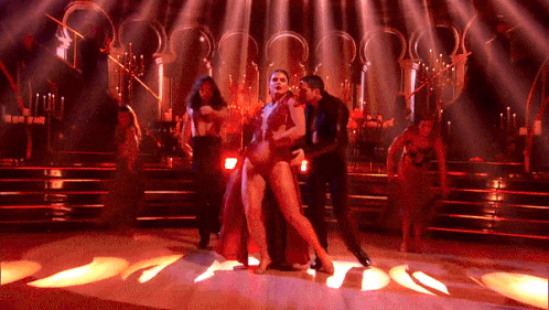 A Woman In A Red Dress Is Dancing With A Man On A Stage GIF