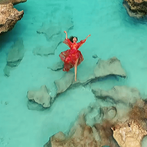 A Woman In A Red Dress Is Floating In A Body Of Water GIF