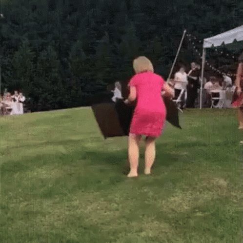 A Woman In A Red Dress Is Holding A Black Umbrella While Standing On A Lush Green Field . GIF
