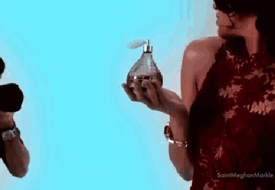 A Woman In A Red Dress Is Holding A Bottle Of Perfume In Her Hands GIF